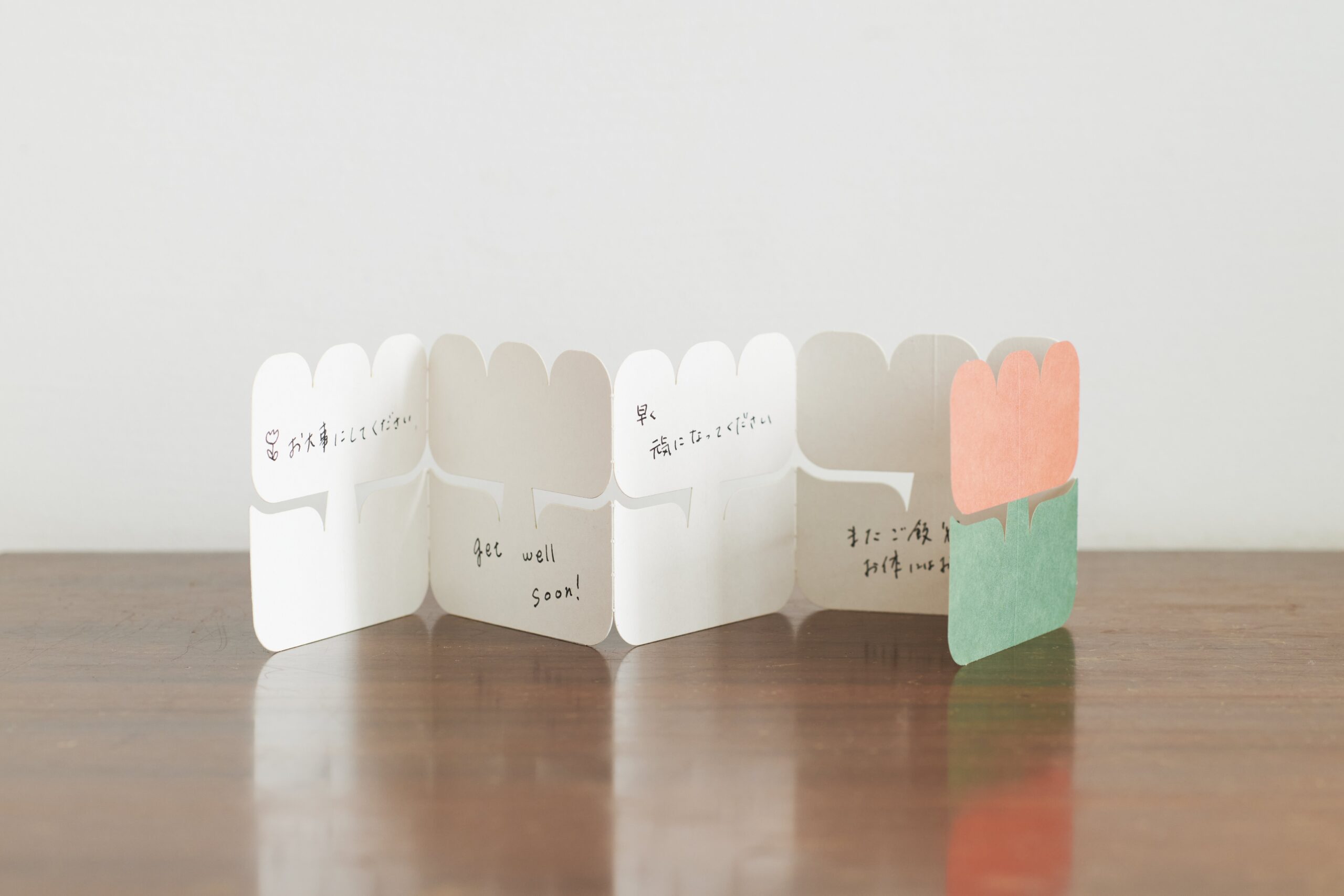 Row of white folded cards with handwritten messages laid out on a wooden table, ending with an orange heart card on the right.
