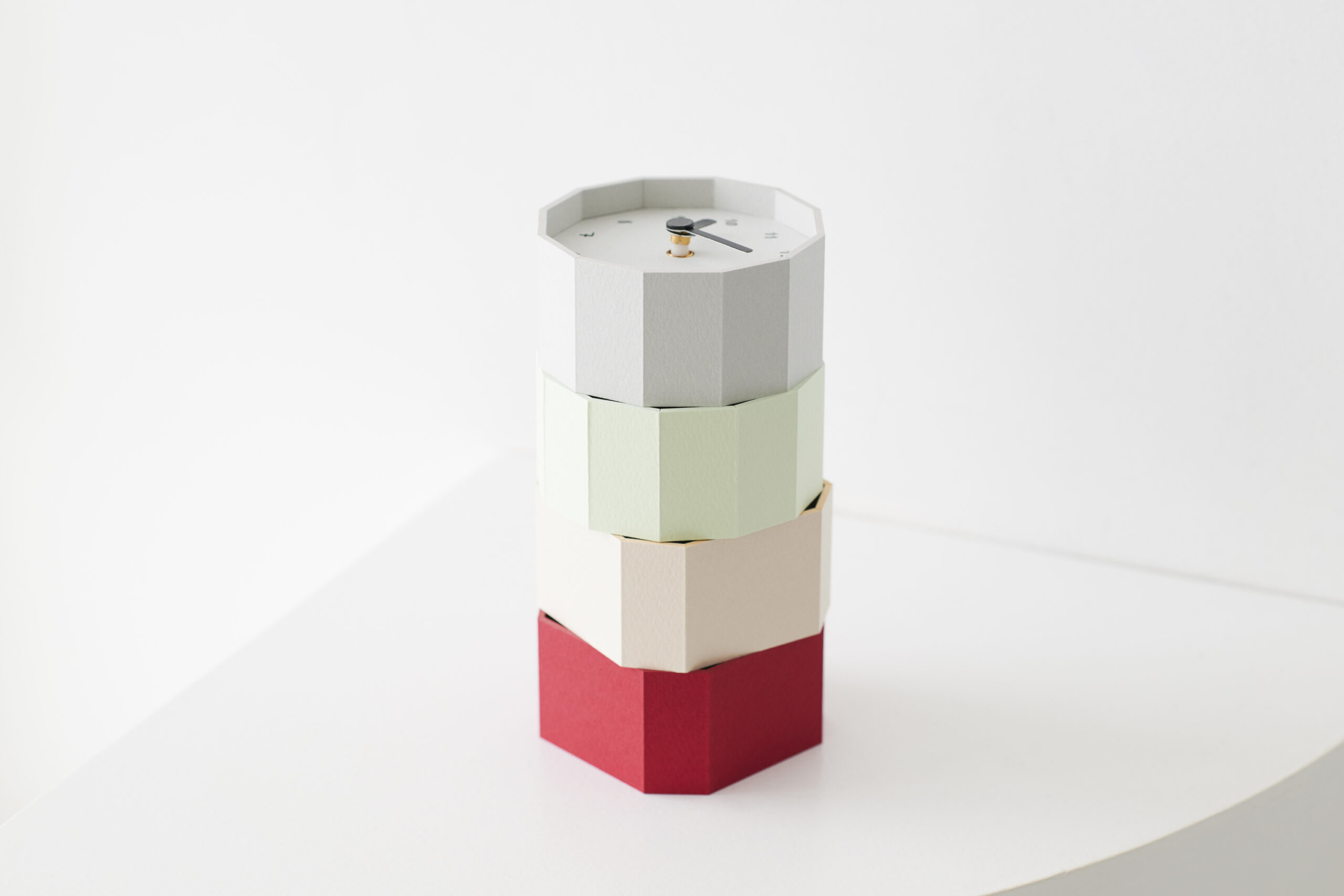 Stack of pastel-colored paper blocks stacked into a tower, with a small white octagonal top featuring a simple clock face and hands at the center.