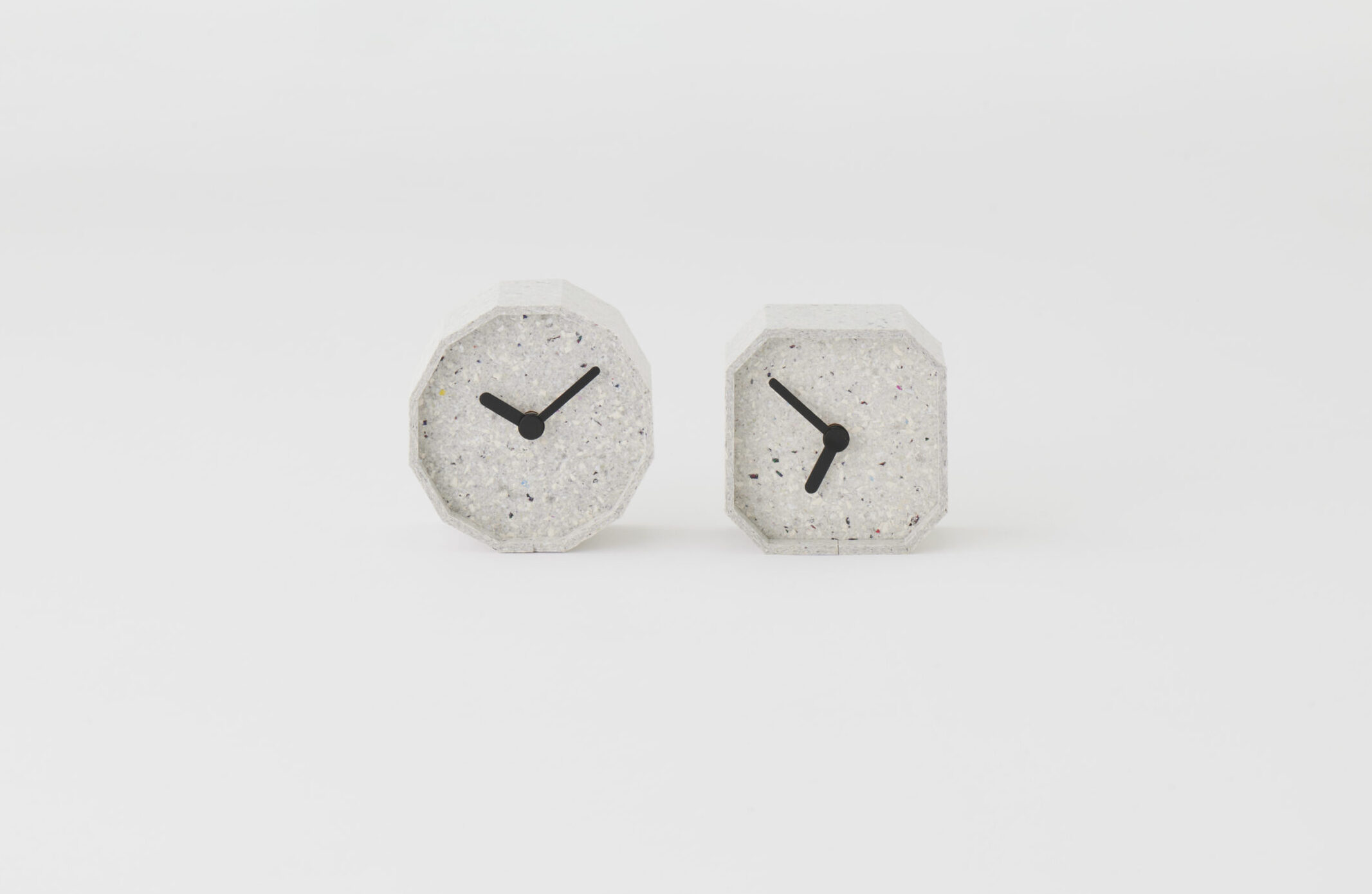Two hexagonal concrete clocks with black hands, placed on a white studio background, showing different times.