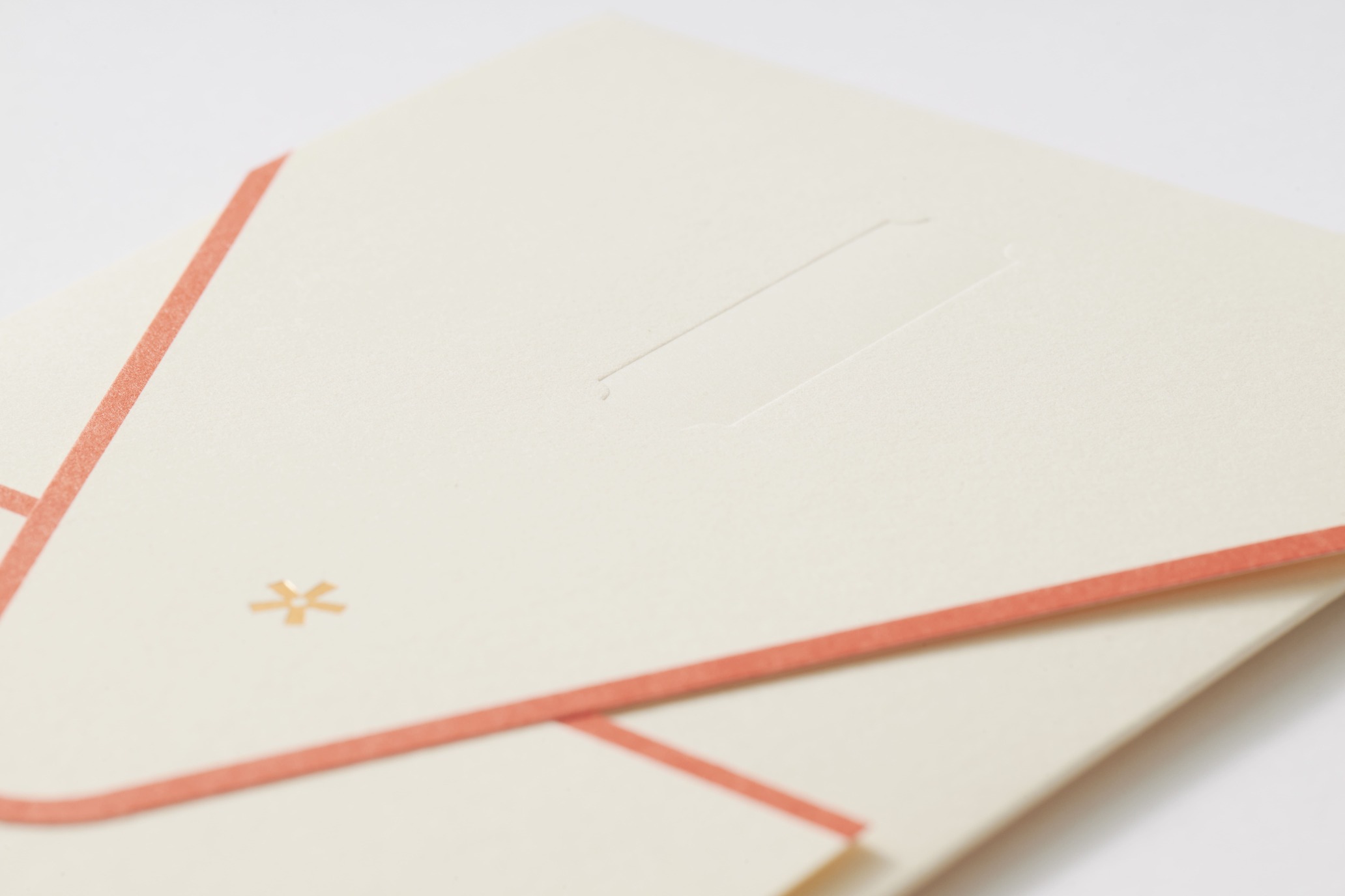 Close-up of cream stationery showing a thin red border and a small gold starburst embellishment.