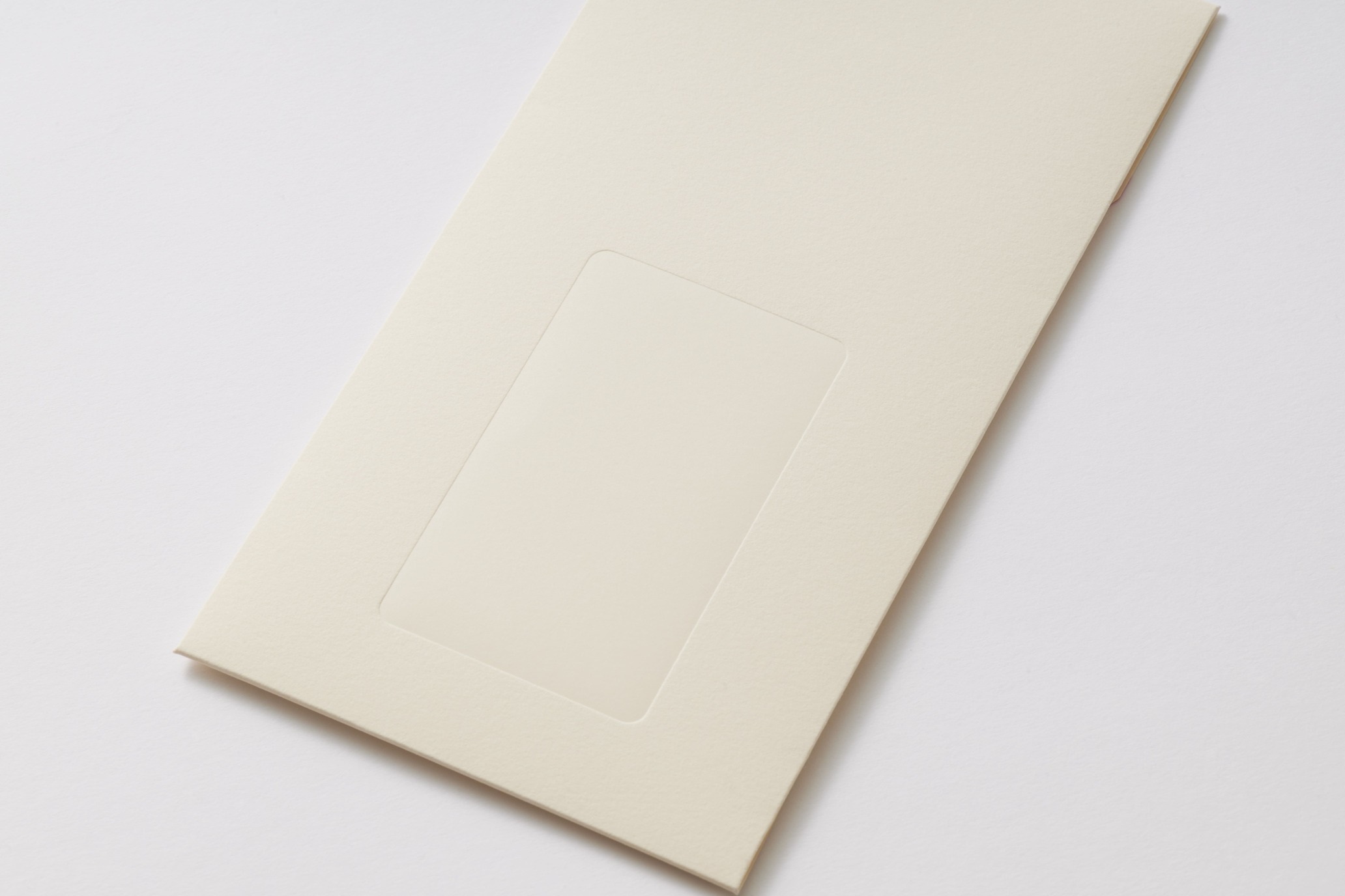 Beige folder or envelope with a rectangular window notch, photographed at an angle on a white surface.