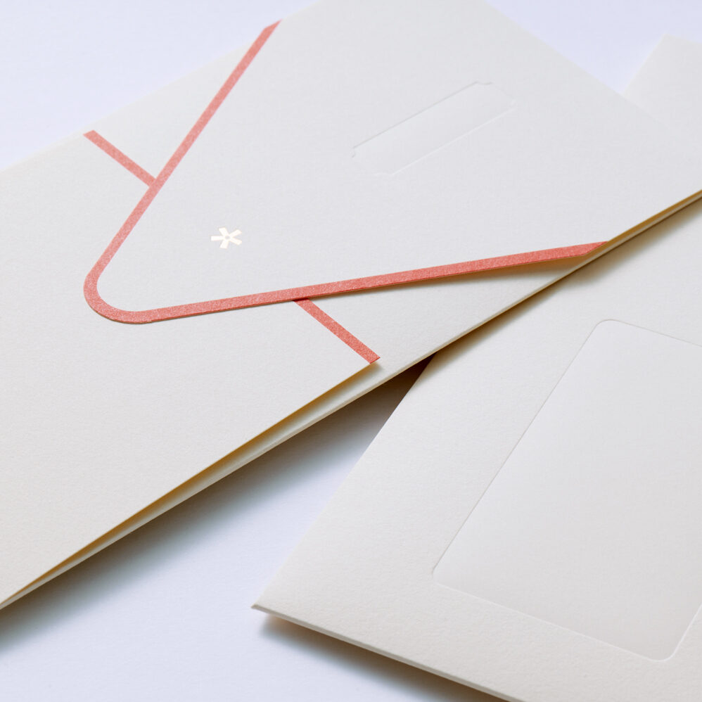 Cream-colored envelopes and cards arranged in a flat lay; a pink decorative line runs along one edge, and the bottom card features a rounded rectangular window.