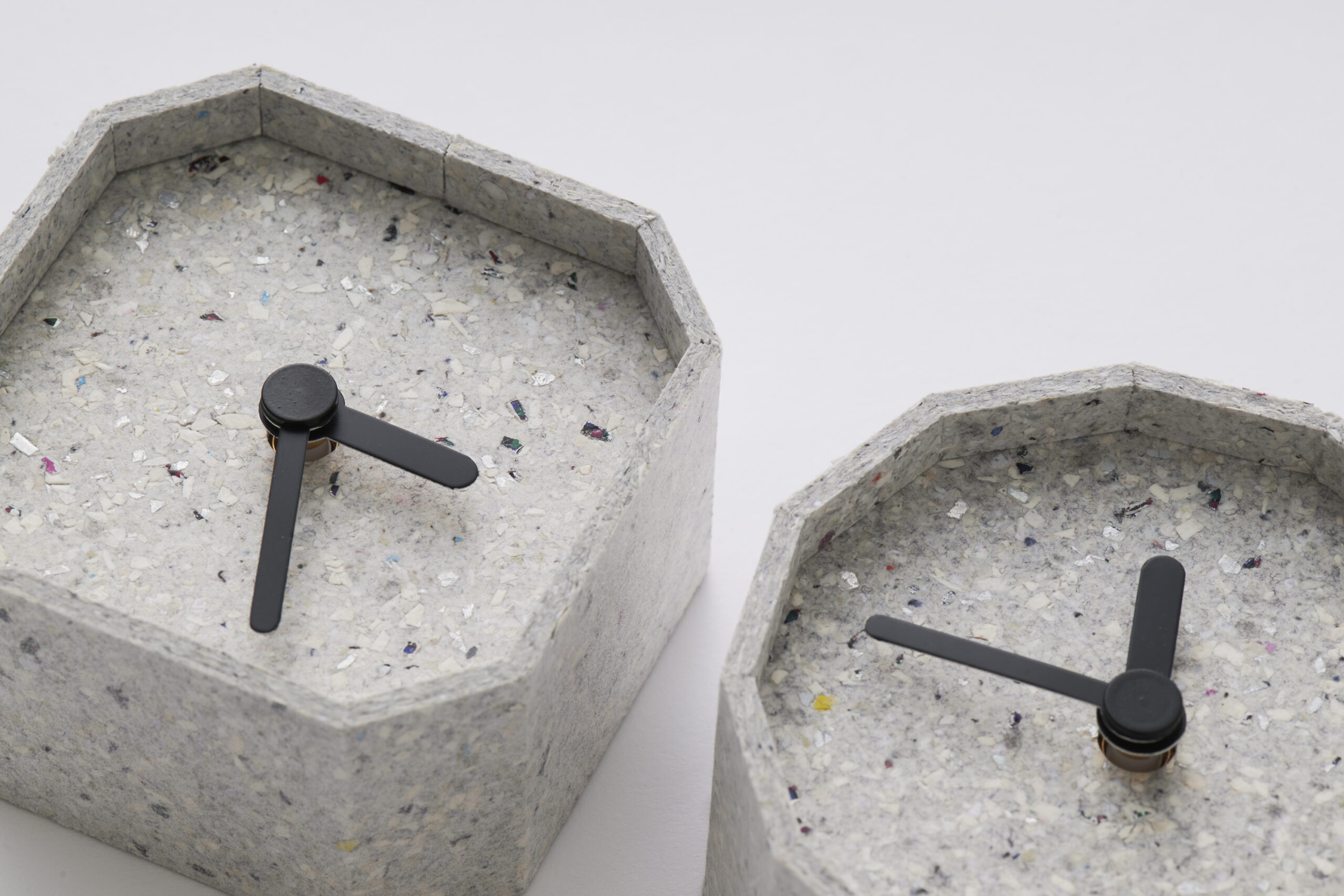 Close-up of speckled terrazzo concrete hexagonal planters with a black metal cross-shaped piece resting on their tops.
