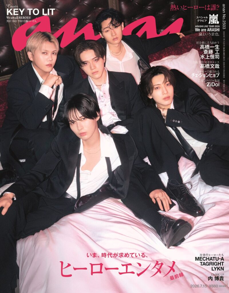 Five young men in black suits lounging on a pink satin bed, posing for a magazine cover with bold pink title text across the top, Japanese captions on the right and bottom.
